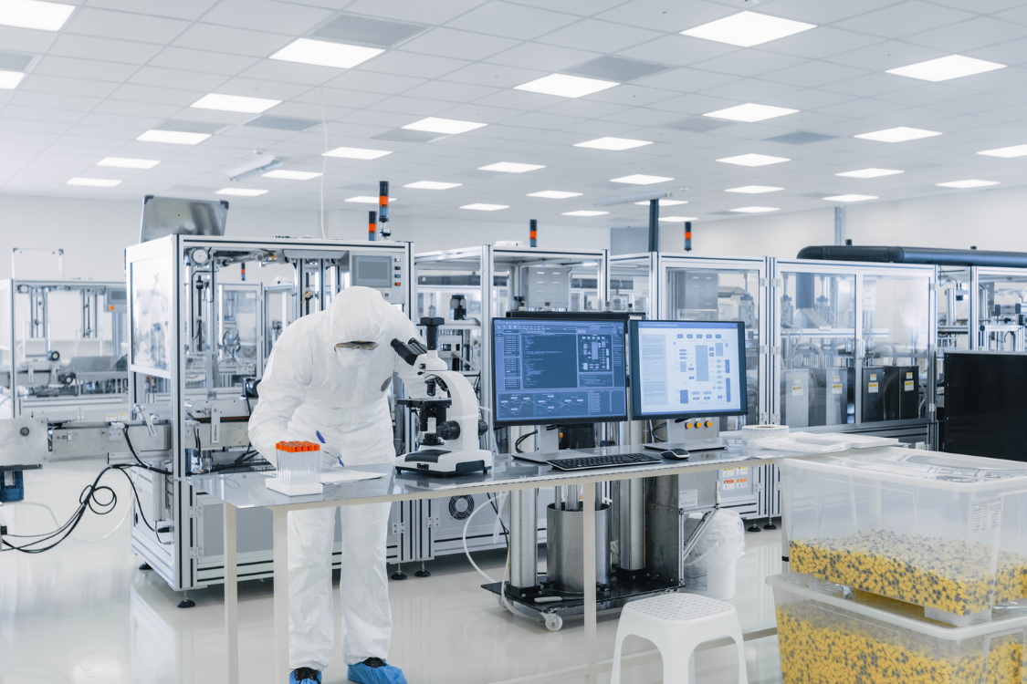 Scientist in cleanroom inspecting supplement samples under microscope at a manufacturing facility.