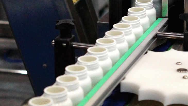 White supplement bottles on an automated production line at a dietary supplement manufacturing facility.