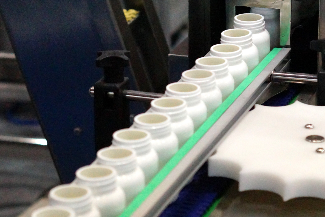 White supplement bottles on an automated production line at a dietary supplement manufacturing facility.