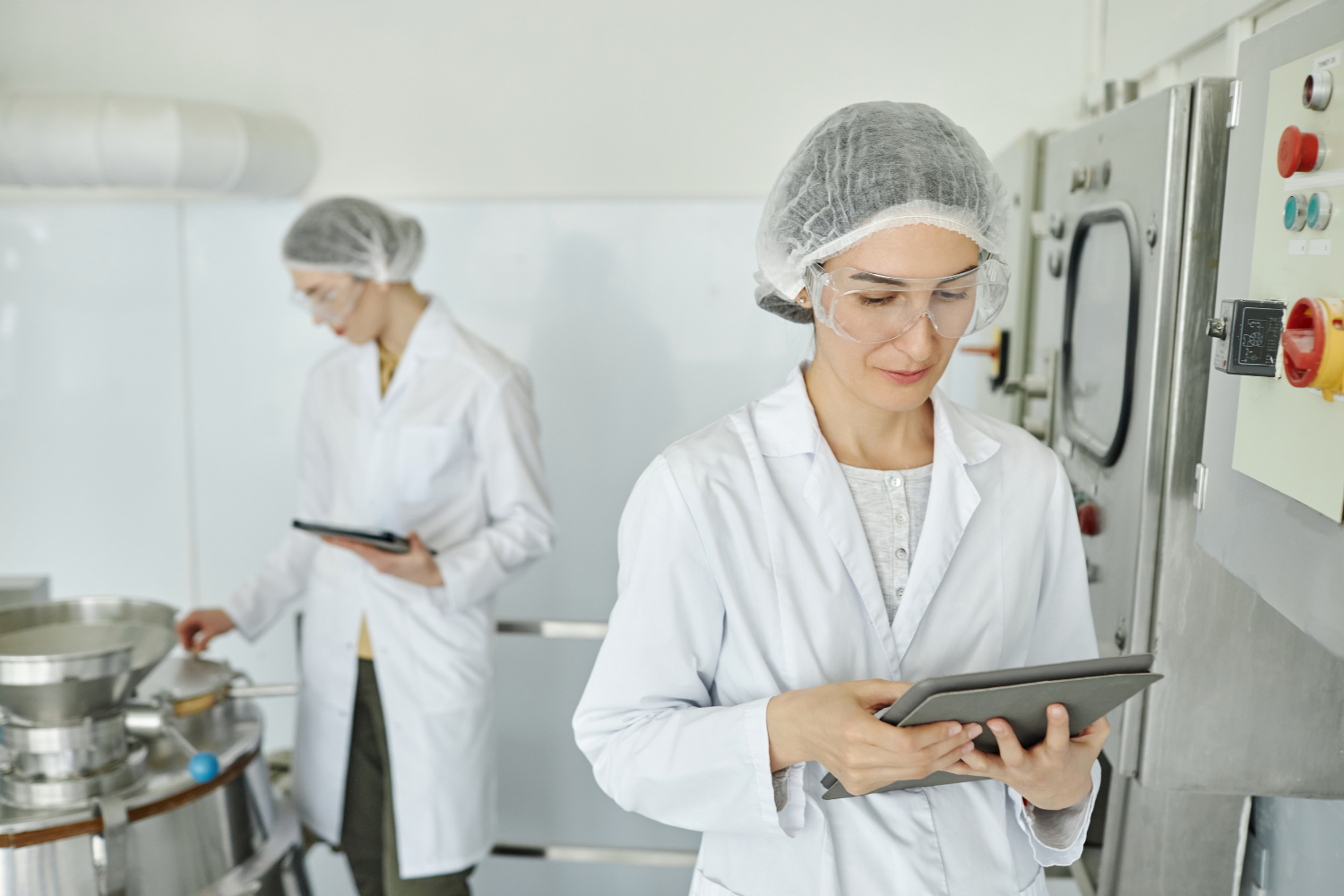 Workers in lab coats with a hair net and clipboard.