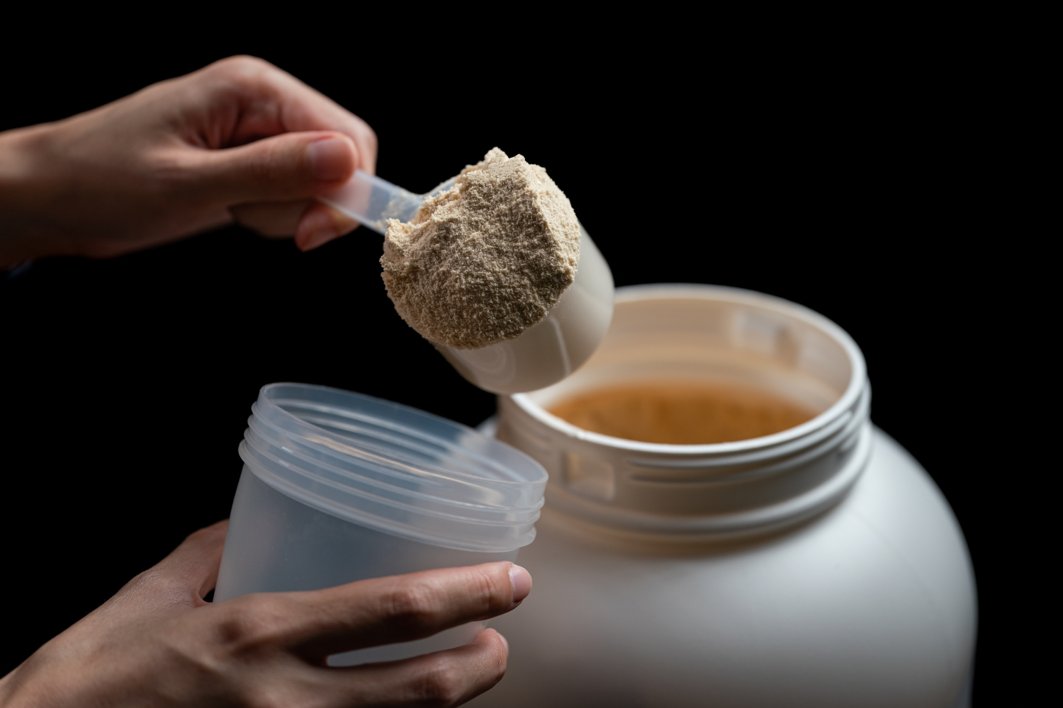 Person scooping protein powder from tub.