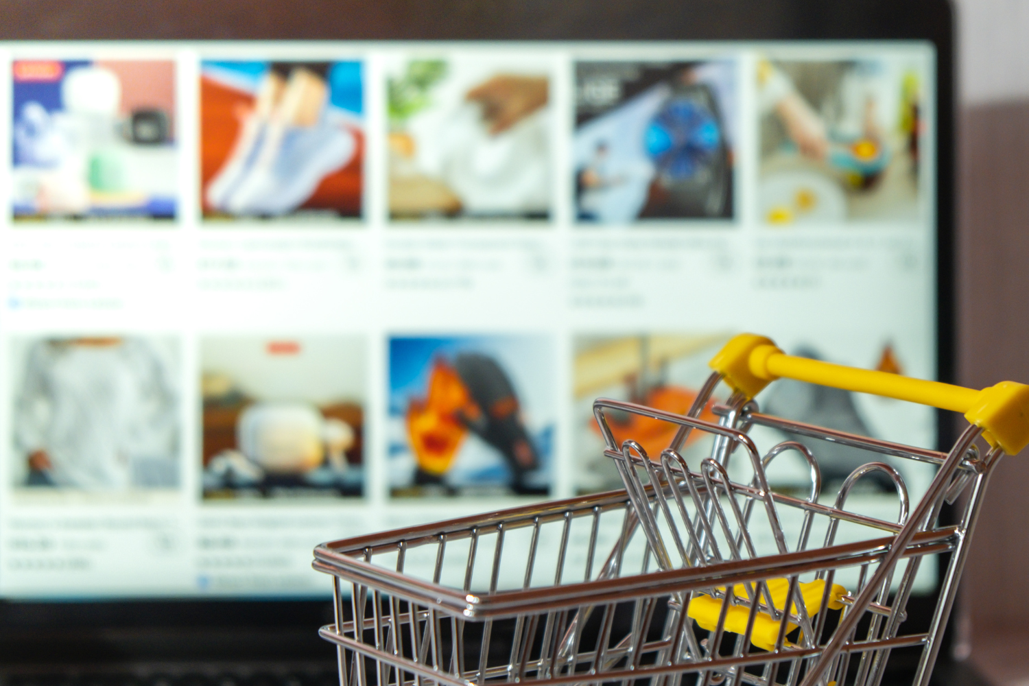 Small shopping cart with online store in the background on a laptop.