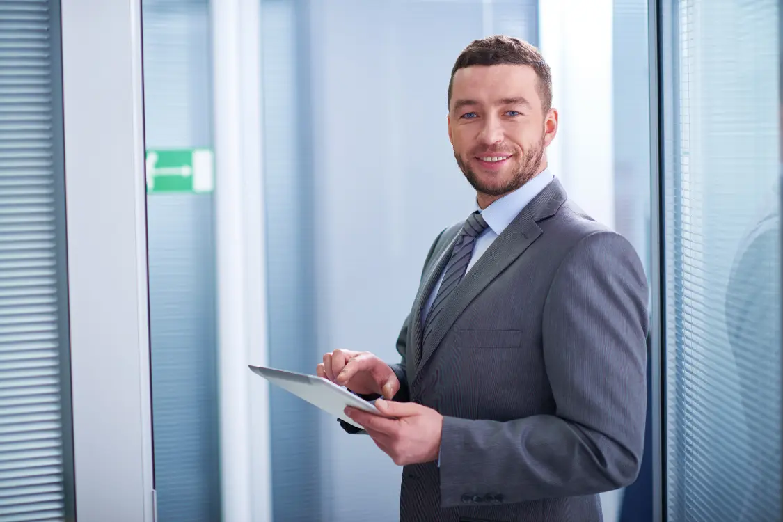 Auditor in suit smiling while reviewing GMP compliance documents on a digital tablet