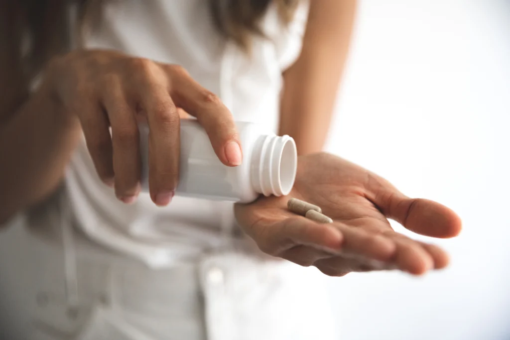 Person pouring supplement capsules from a bottle into hand