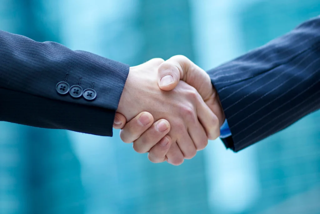 A close-up of two business people shaking hands, emphasizing the transparency and trust needed in a long-term manufacturer partnership.