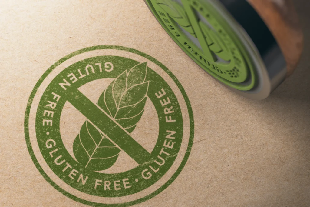 Close-up of a rubber stamp applying a green gluten-free circle symbol with a crossed-out leaf onto a brown surface, representing documented gluten testing by a supplements manufacture.