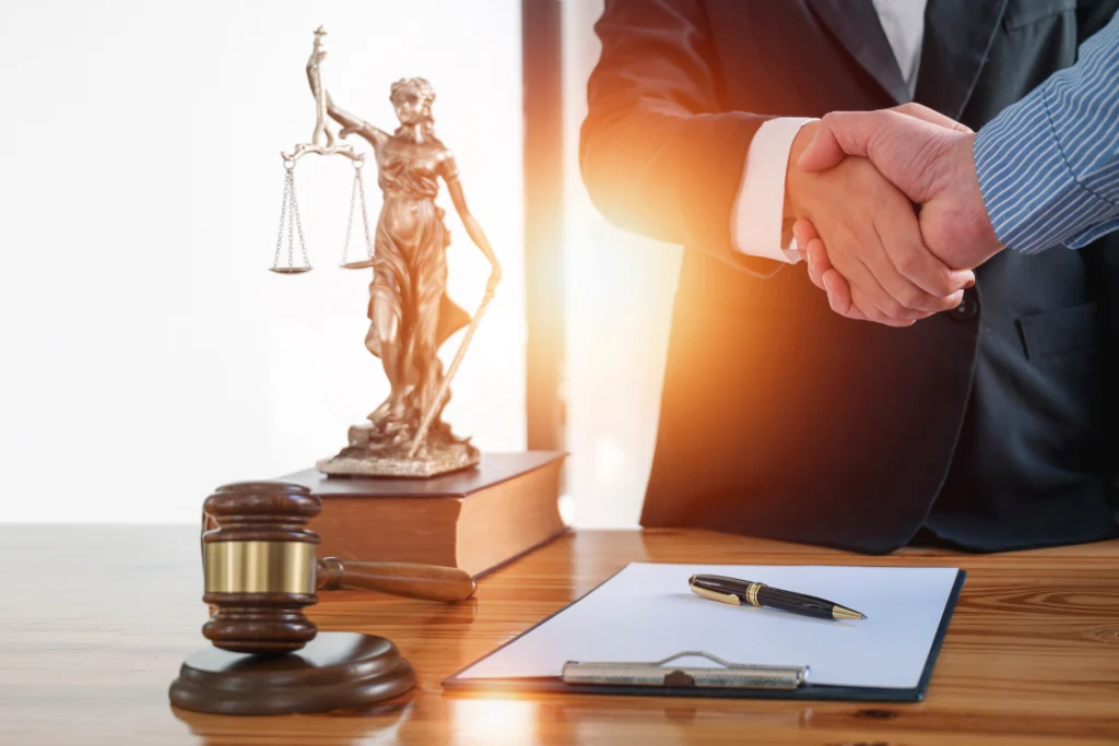 A handshake over a wooden desk with a gavel and a statue of justice, representing a legal agreement and the importance of regulatory compliance supplement transparency.