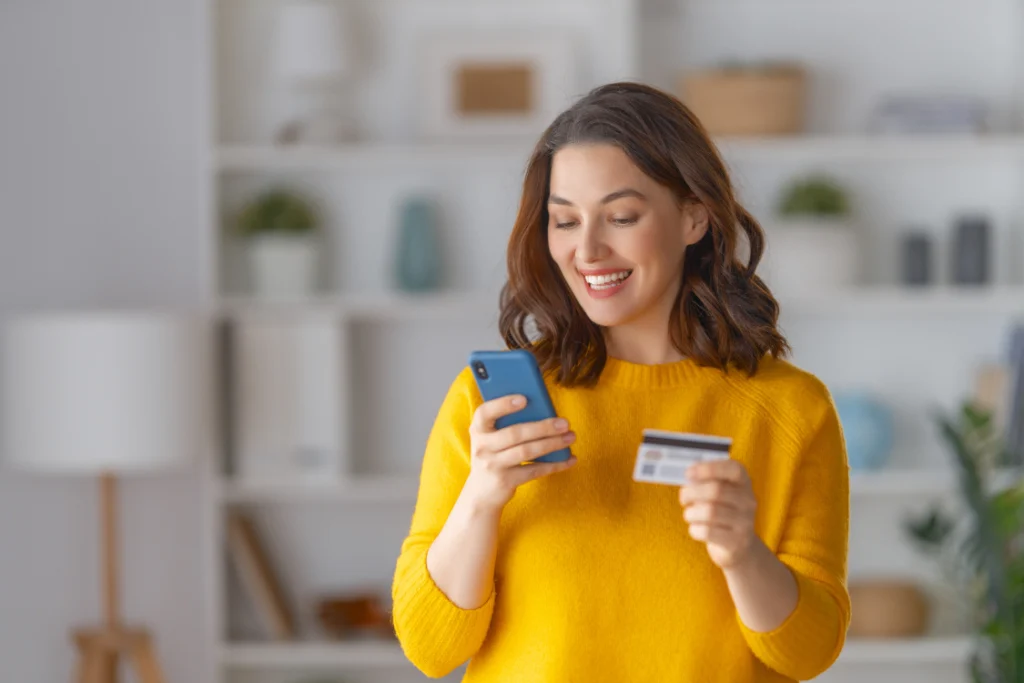 Happy woman smiling while holding a credit card and phone, illustrating the ease of making an online purchase of staggered ordering supplements.