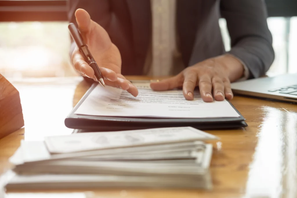 A person pointing to a contract with money in the foreground, signifying the financial and legal due diligence required for a supplement partnershi