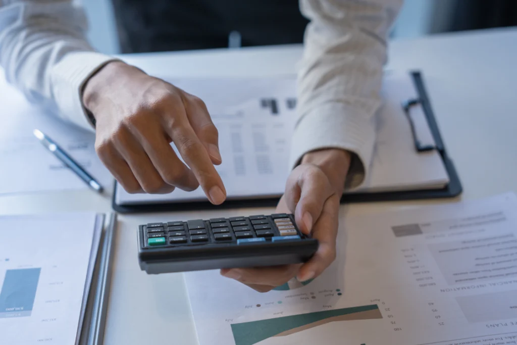 Person using a calculator to review supplement manufacturer pricing comparison data and budget reports.