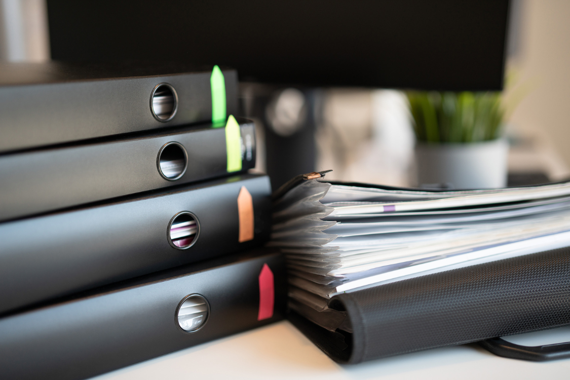Stacked black binders and folders with colored tabs, representing the organization of supplement manufacturer public records for review.