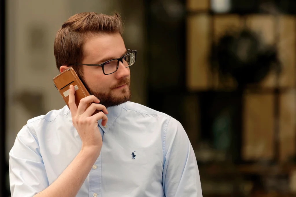 A man with glasses and a beard on a phone call, vetting a partner using information from supplement manufacturer public records.