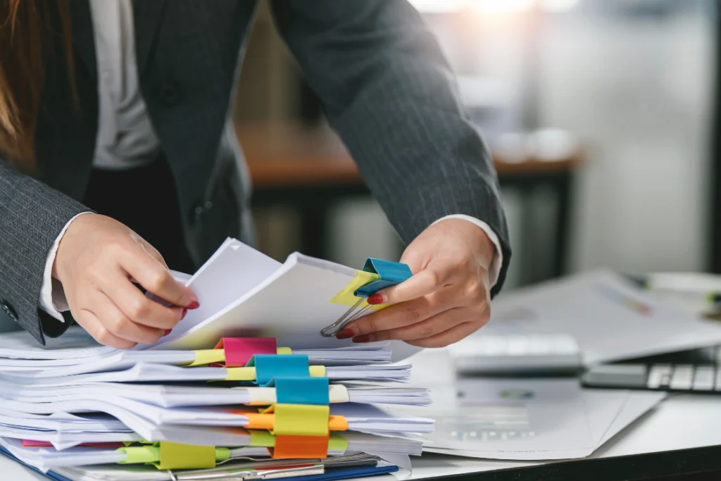 A person organizing stacks of documents with colorful binder clips, representing the due diligence process of reviewing supplement manufacturer public records.