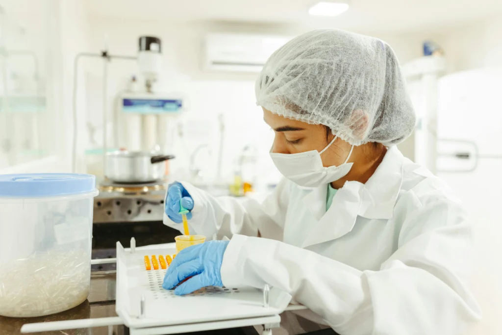 Scientist in lab coat and gloves conducting quality check on a supplement pilot production run by filling capsules on a tray.