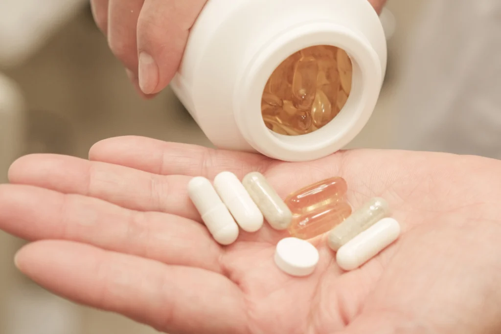 Hand holding assorted supplement pills and capsules, poured from a white bottle, to represent the final consumer product.