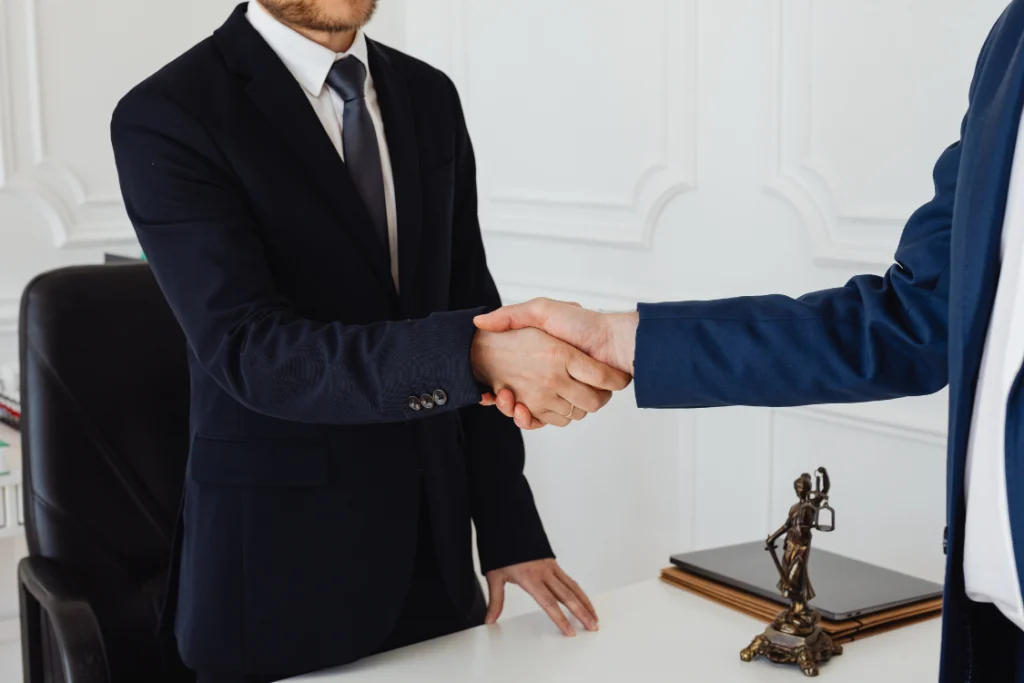 A handshake between two individuals in business suits over a desk with a contract, symbolizing the final stage of a supplement manufacturing agreement and the start of a successful partnership with experienced manufacturers for consistent quality of finished products.