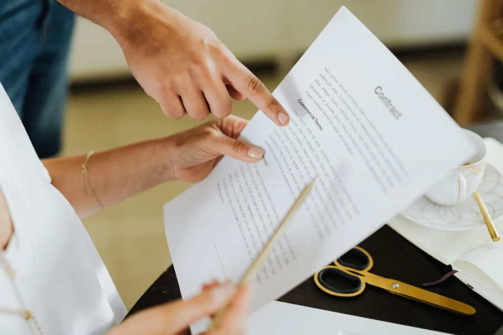 Close-up of a finger pointing to commercial terms on a contract, highlighting the importance of reviewing the details of a supplement manufacturing agreement to ensure the manufacturer complies with safety standards for product quality.