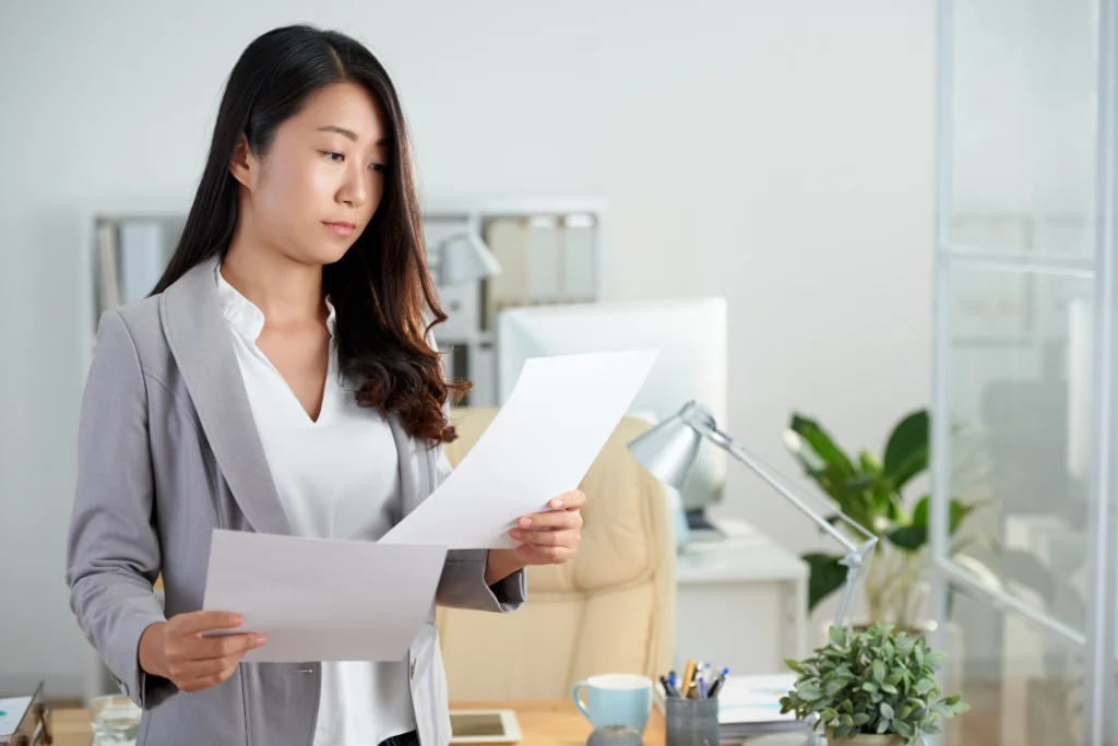 Asian businesswoman reviewing documents or a contract in an office setting, representing the process of checking documentation for a supplement manufacturer checklist.