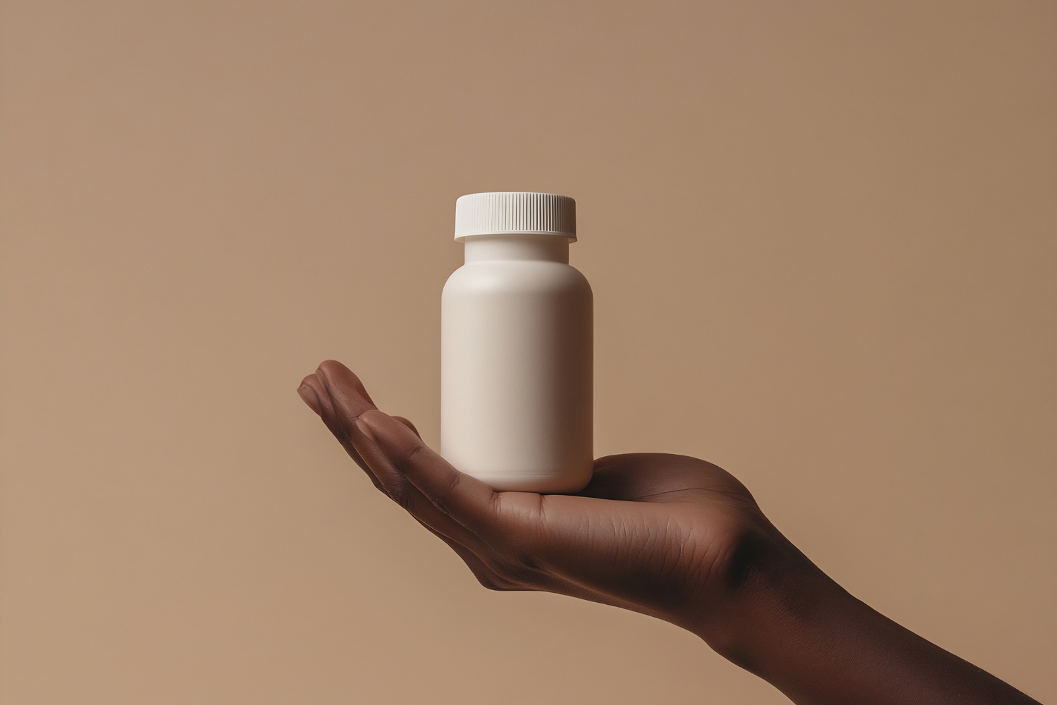 A hand with dark skin tone holding a plain white, unbranded supplement bottle against a beige background, representing private label product choices for those learning how to start a supplement company.