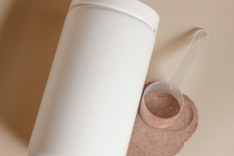 A white tub container next to a scoop filled with brown powder.