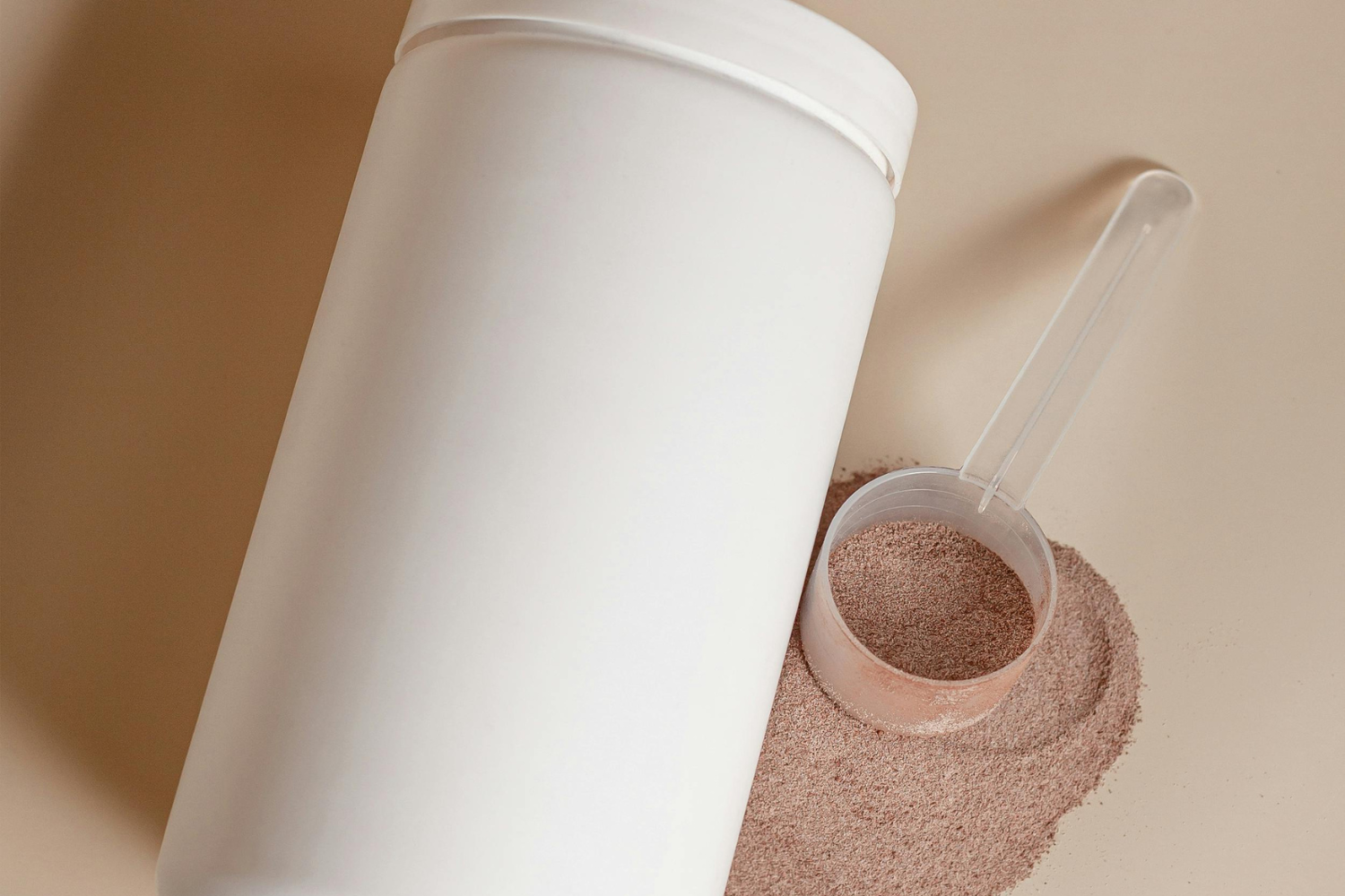 A white tub container next to a scoop filled with brown powder.