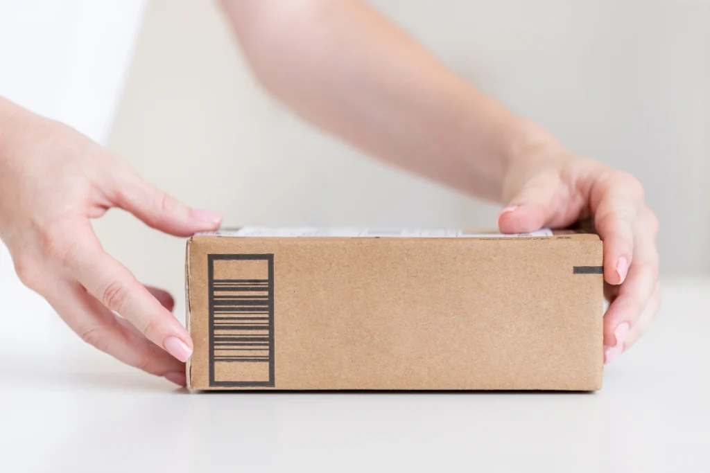 A person's hands holding a simple, brown shipping box with a barcode, representing the final delivery stage of private label dropshipping supplements.