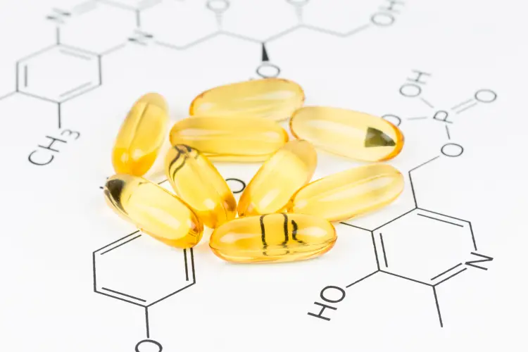 Close-up of yellow softgel capsules (omega-3 or fish oil) resting on a diagram of a chemical structure, symbolizing the importance of formulation and ingredients for how to start a supplement company.