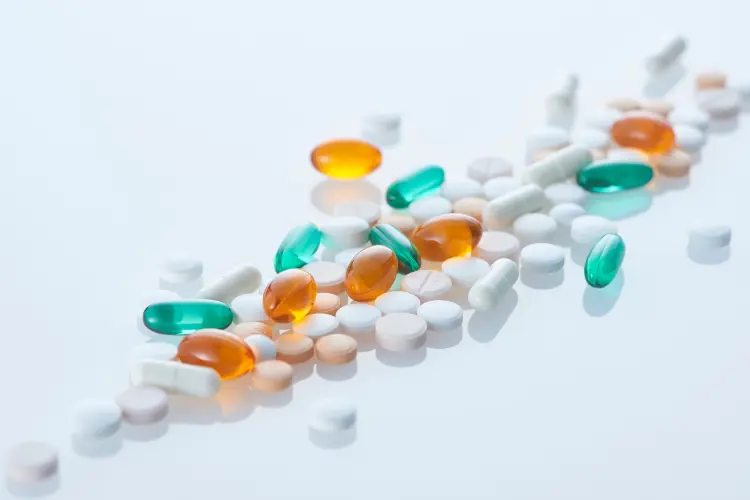 A spread of various colored and shaped supplement pills and capsules, including white tablets and green/orange softgels, illustrating product options when learning how to start a supplement company.